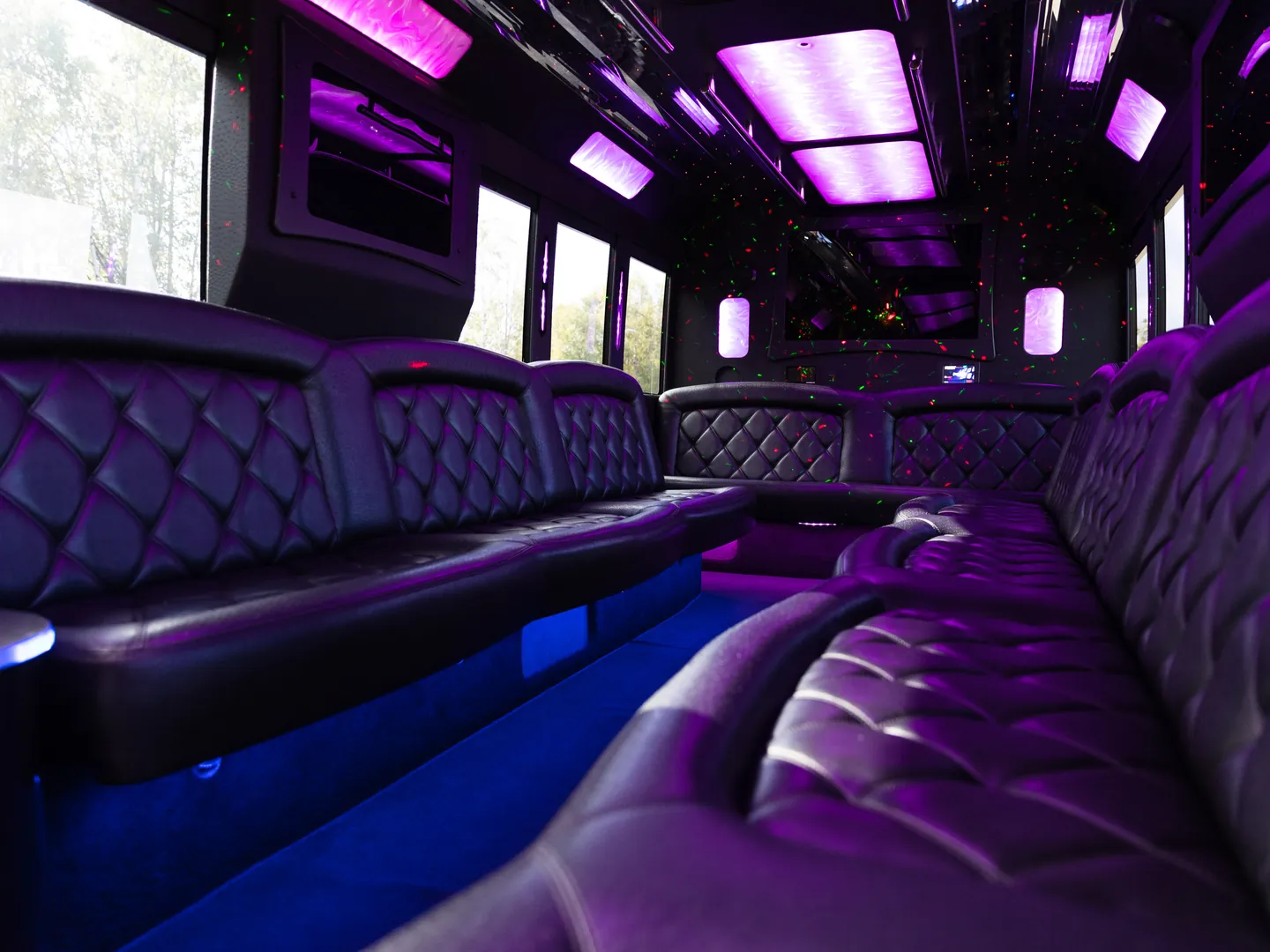 BAC party bus interior in purple and blue light, with quilted leather seating along both sides