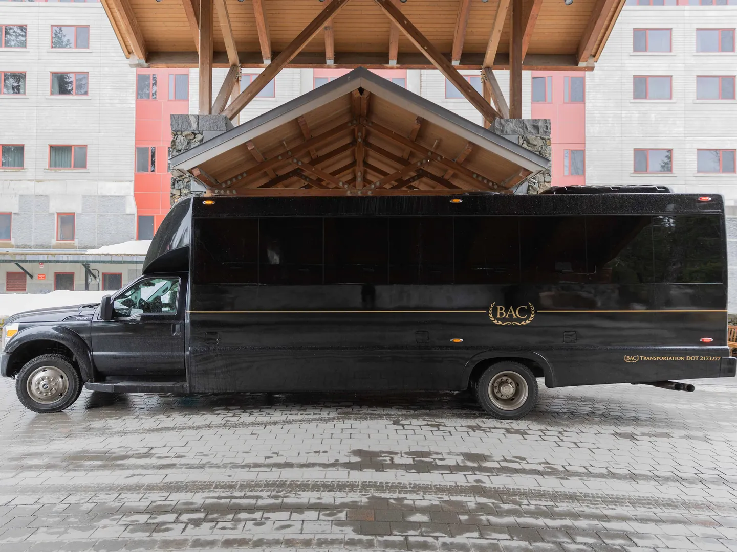 A black BAC limo bus waiting under the timber entrance of a mountain resort hotel